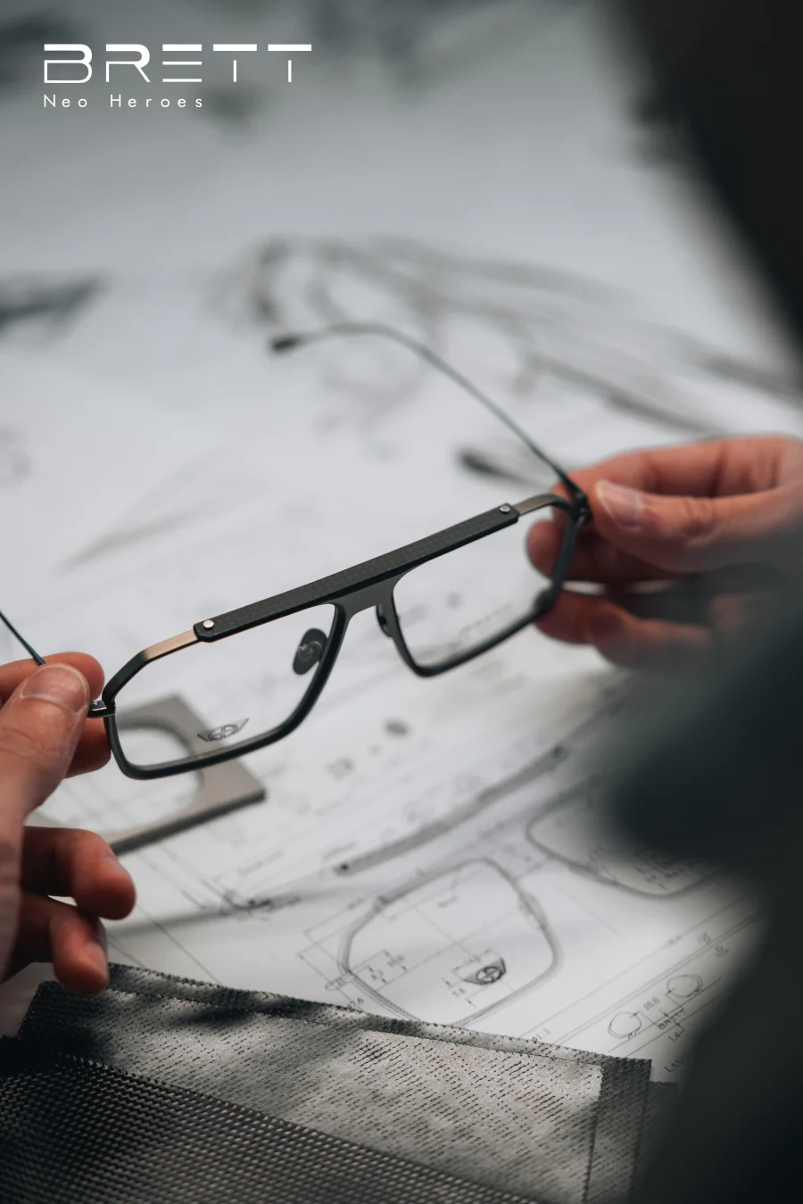 Brett Eyewear Brillenfassung in der Hand vor technischem Entwurf – inspiriert von Motorsport und Präzision